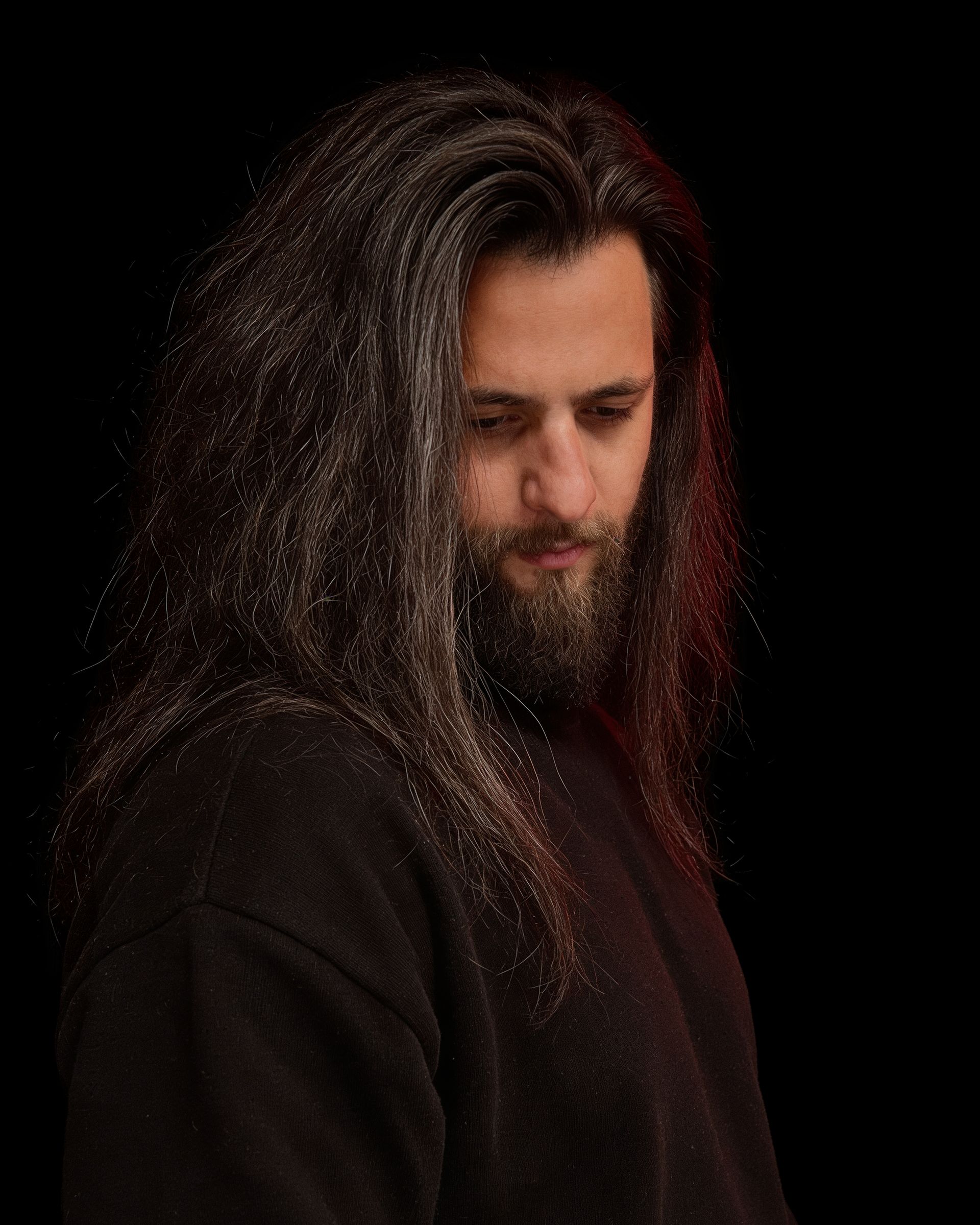 Daniel Costrasel turned away in the dark, looking down, the length of his hair caught by one warm light.